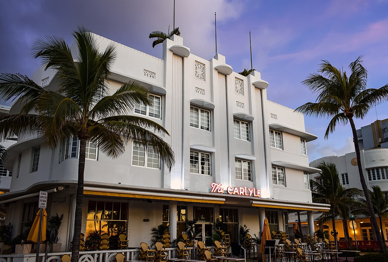 Upward diagonal view from the left of the east facade of the building The Carlyle in the Art Deco District of Miami Beach, captured during the blue hour in the early morning. The photo shows the chara