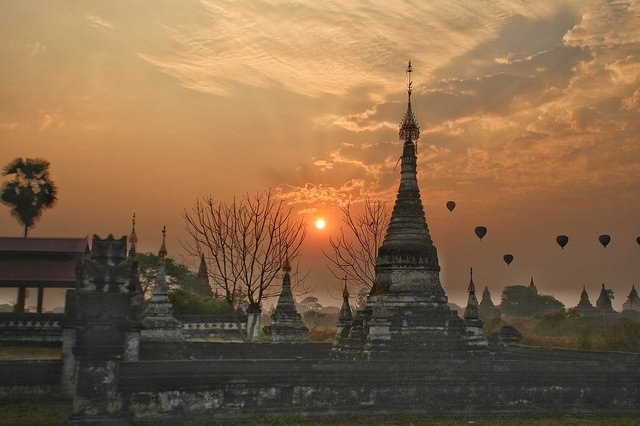 Hot air balloons floating over Bagan temples at sunrise with golden light on the horizon.