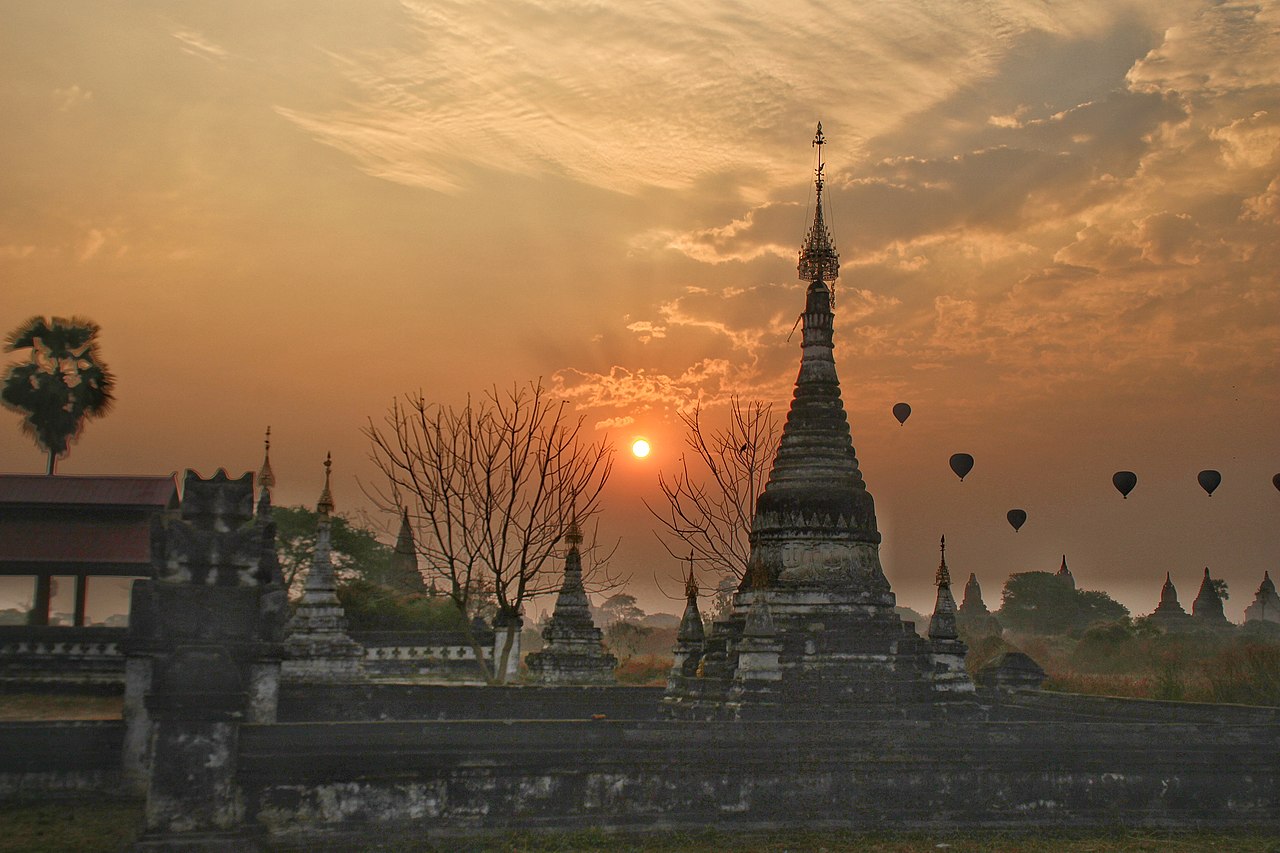 Hot air balloons floating over Bagan temples at sunrise with golden light on the horizon.