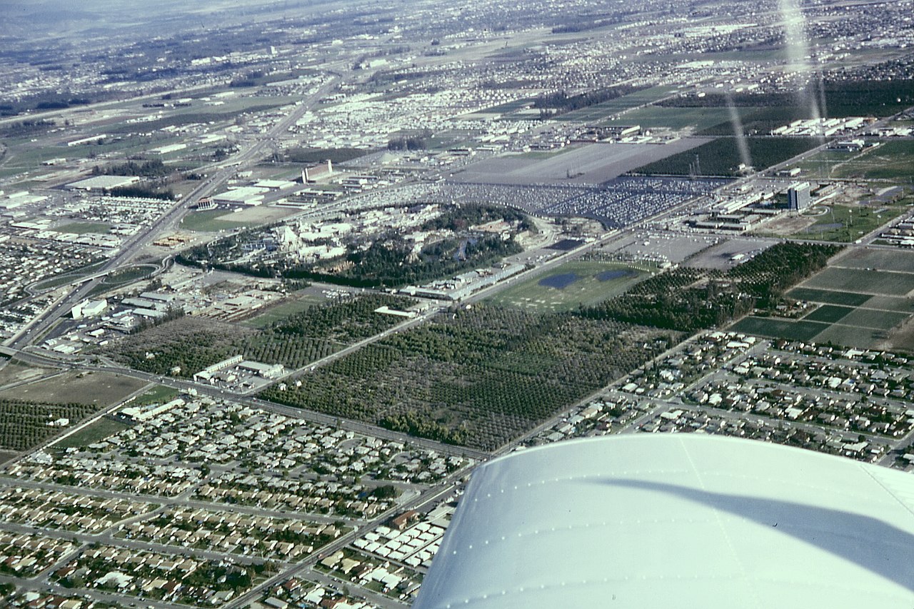 Archival aerial photo of Anaheim, California including Disneyland, the Disneyland Hotel, and the monorail system. The Disneyland Heliport, surrounding orange groves, Santa Ana Freeway (now I-5) and th