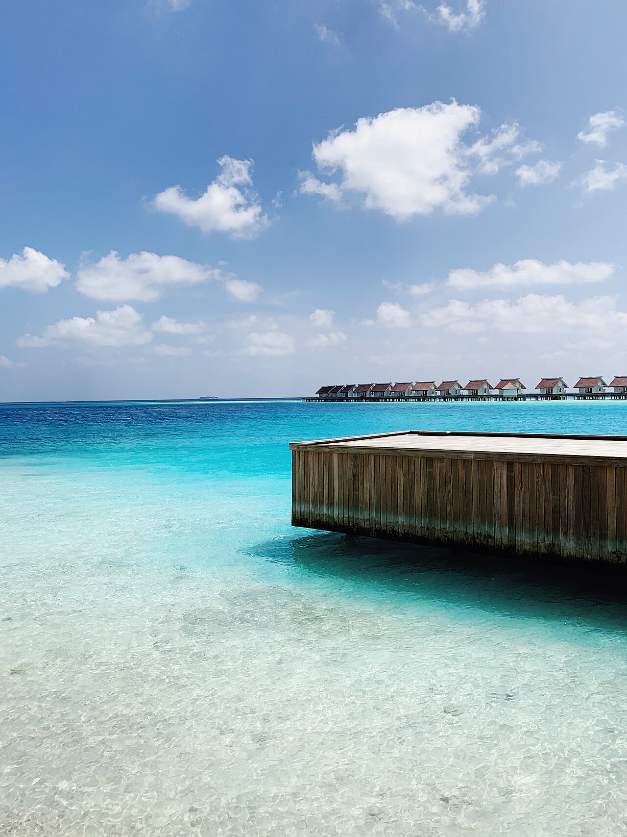 The image shows overwater bungalows surrounded by blue oceans.