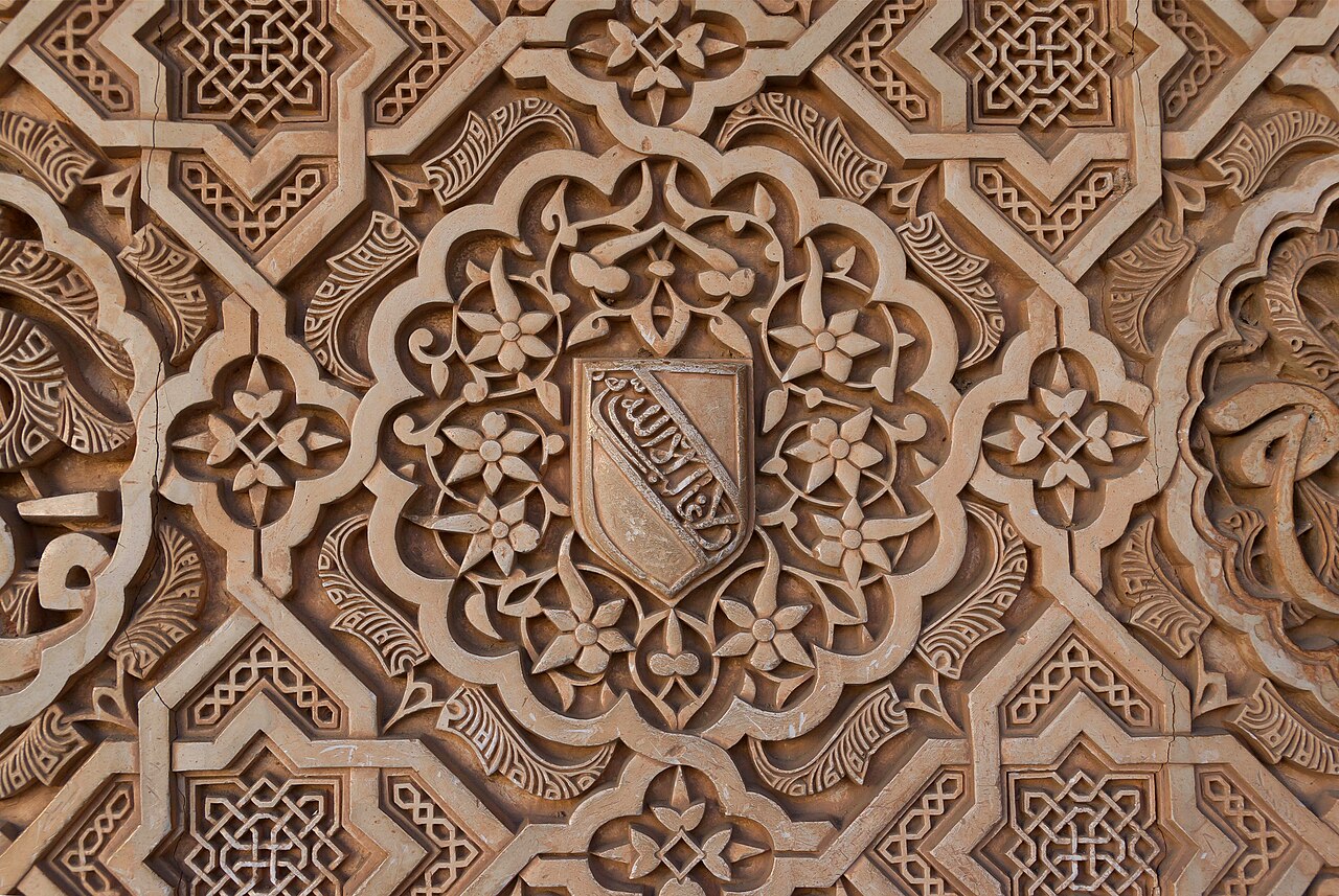Escutcheon with the nasrid kings motto, Wa lā gāliba illā-llāh (ولا غالب إلا الله),And nobody is victorious, but God, stucco on the walls of the Alhambra, 13th-century, Granada, Spain.