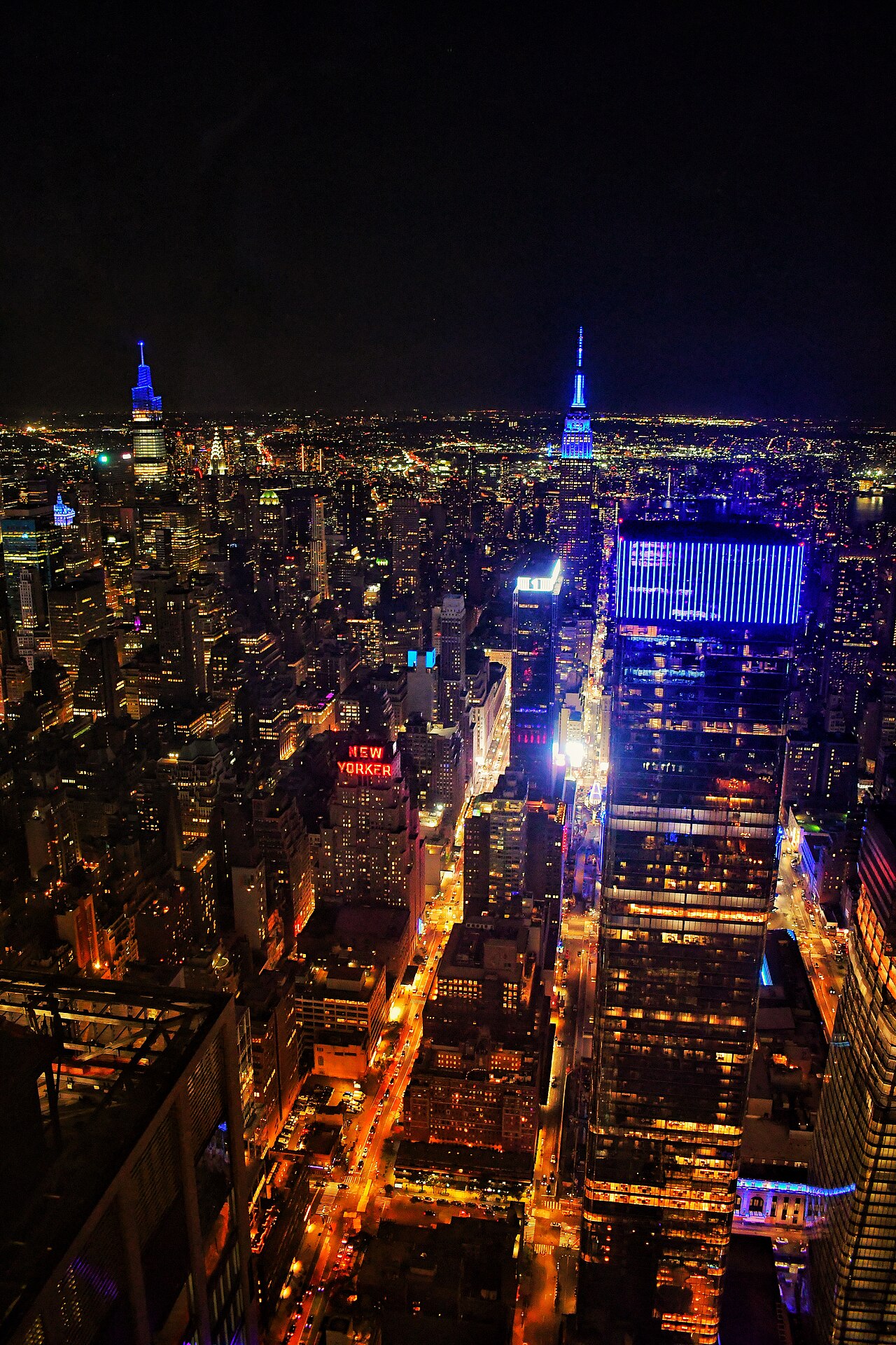 An aerial view of New York City at night, with the Empire State building lit up in blue.
