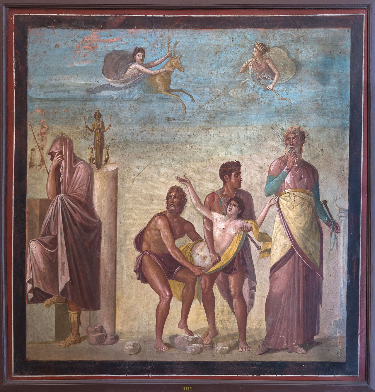 Iphigeneia carried to the sacrifice (centre) while the seer Calchas (on the right) watches on and Agamemnon (on the left) covers his head in sign of deploration. In the sky, Artemis appears with a hin