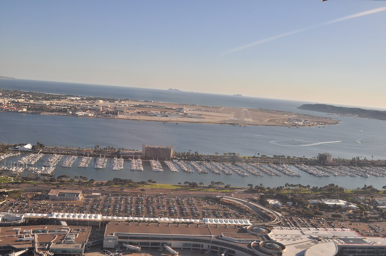 Low aerial from over San Diego International Airport, San Diego, California (terminals partly visible in foreground), looking south across North San Diego Bay to Naval Air Station North Island on Coro