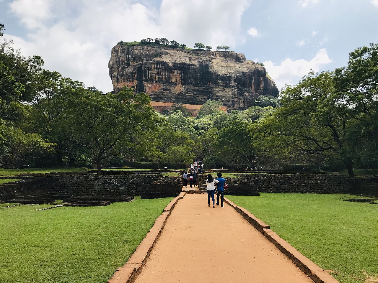 Front view of Sigiriya Lion Rock fortress rising above the tree canopy, seen from ground level.