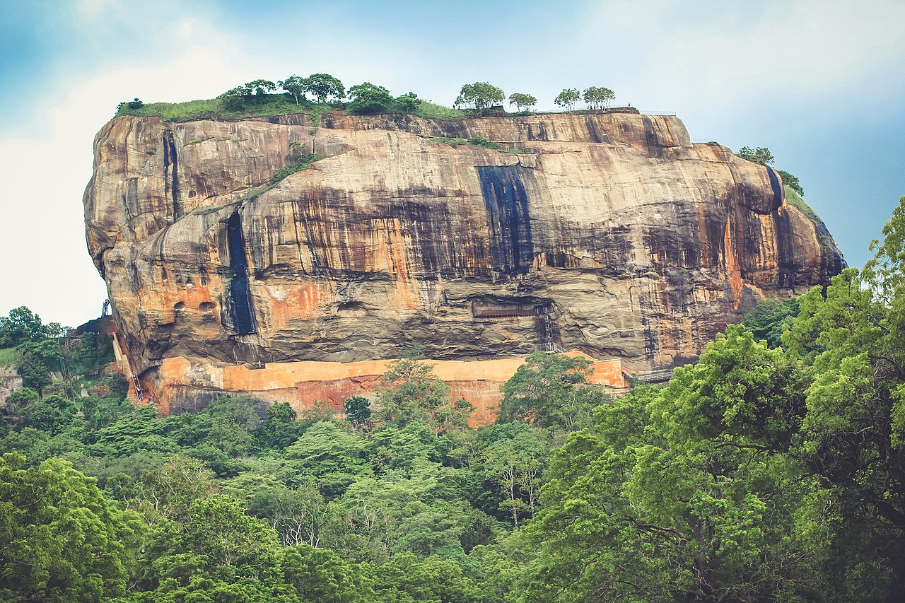 Sigiriya ancient rock fortress viewed from a distance, showing the full height of the granite column against a cloudy sky.