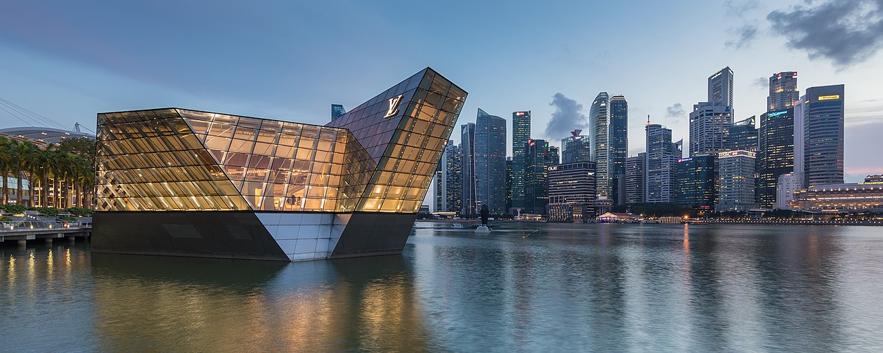 Illuminated polyhedral building Louis Vuitton over the water at Marina Bay in the evening, with skyscrapers of the Central Business District in the background, Singapore